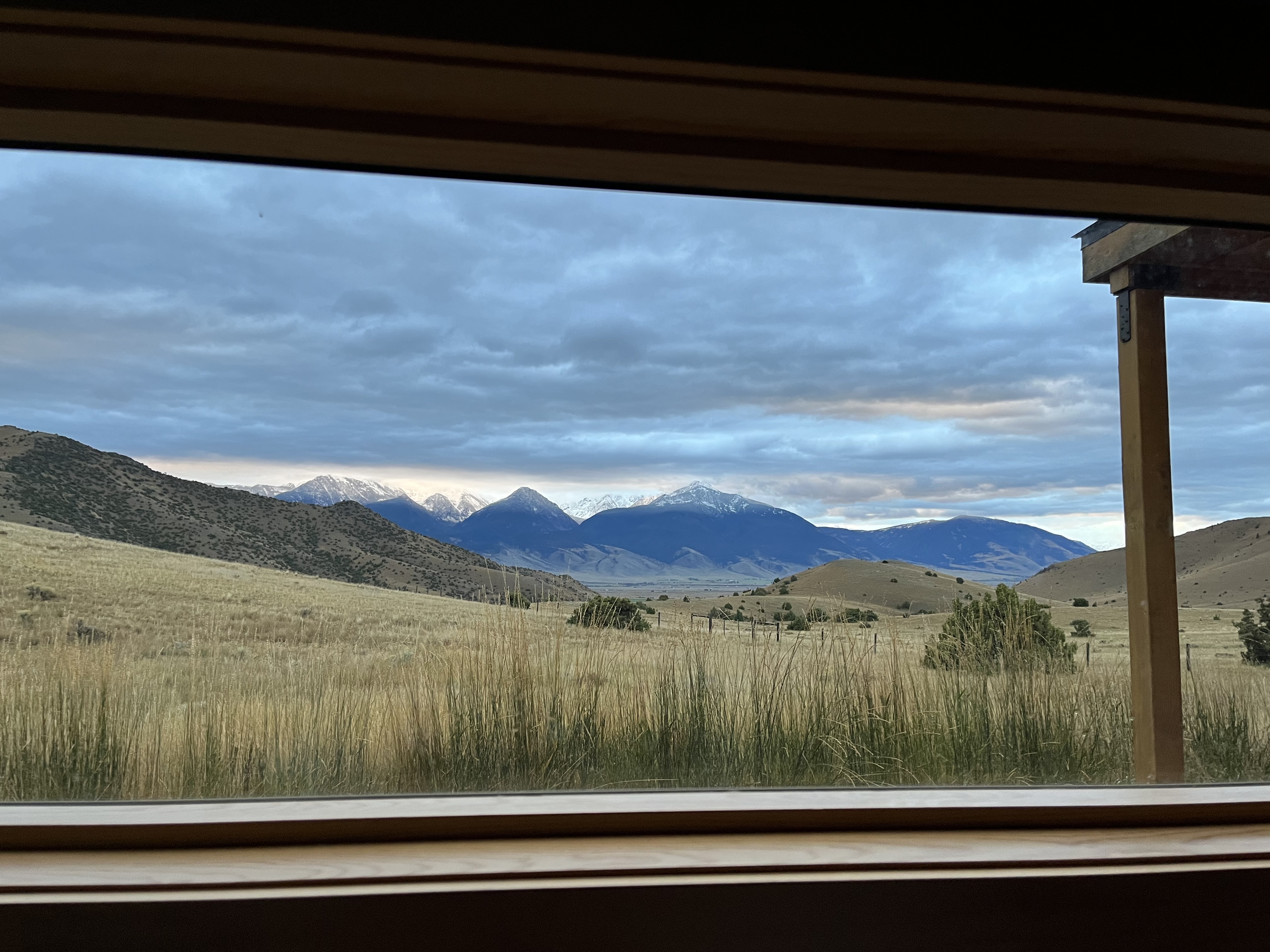 View from a window of snow-capped mountain peaks against a cloudy sky