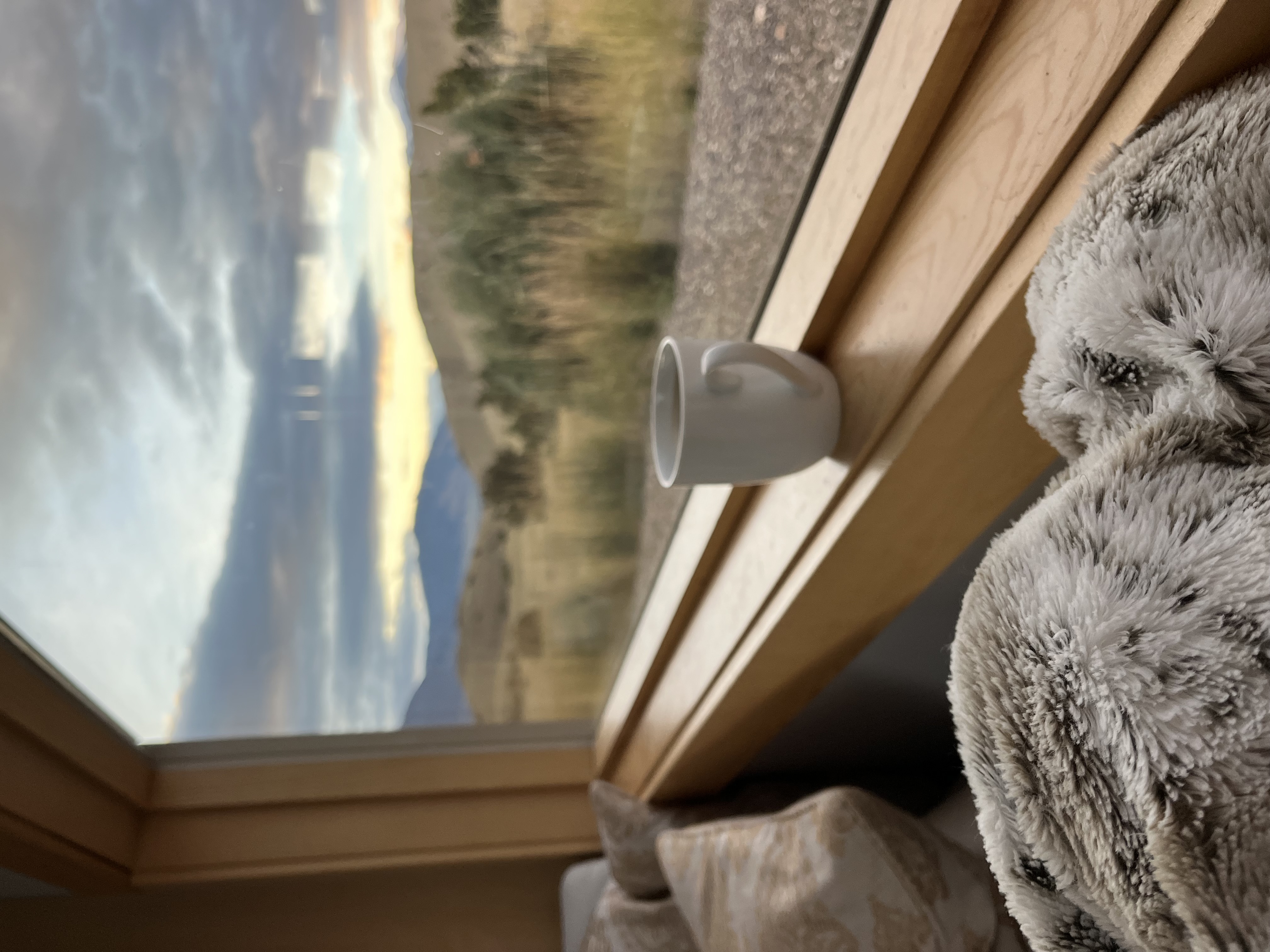 View from a window of snow-capped mountain peaks against a cloudy sky, but this time with a cup of coffee on the windowsill