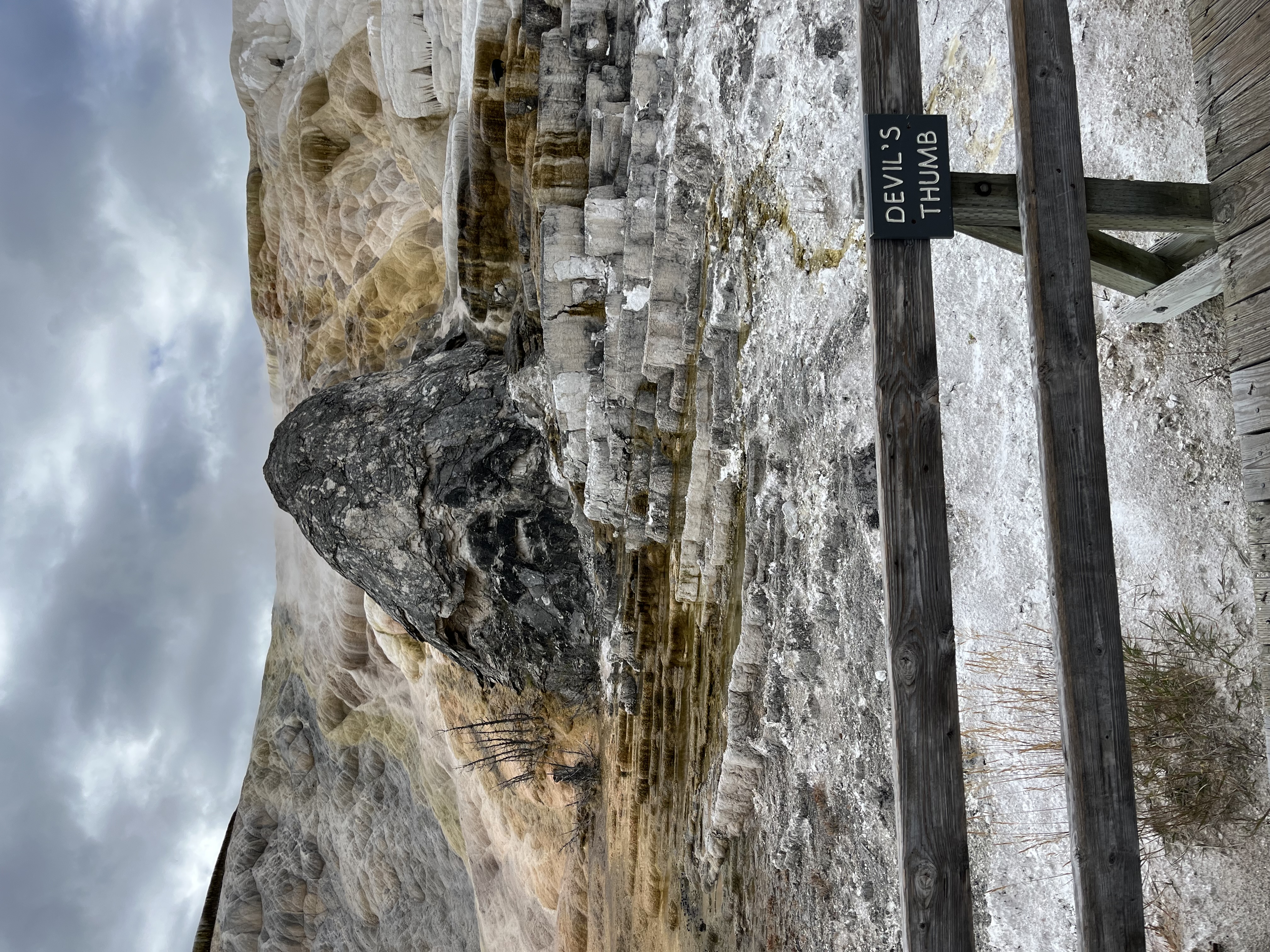 White, brown, and gray steaming rock formations with a sign labeling part of it as "Devil's Thumb"