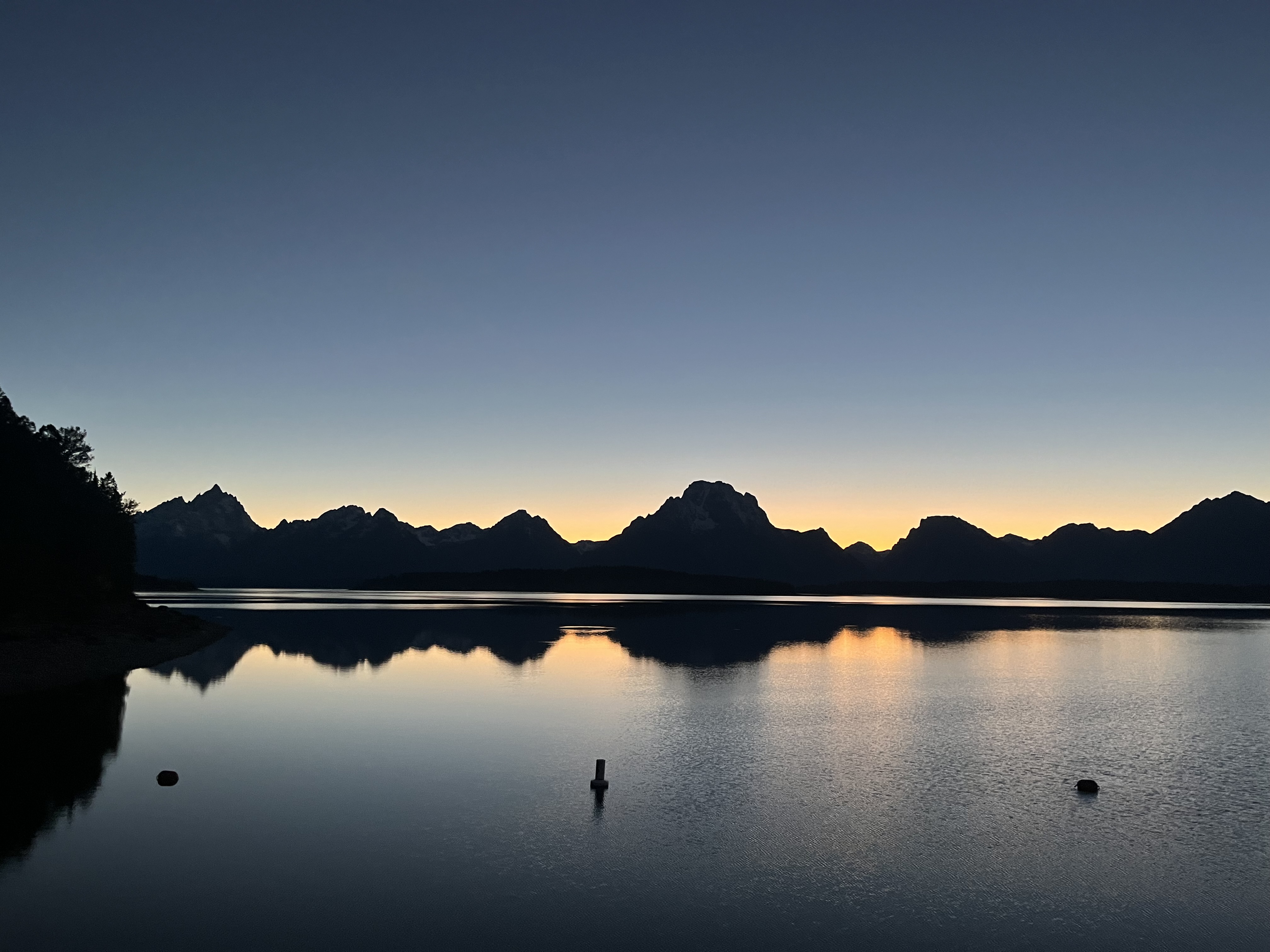 Sunset behind the mountains, creating a dark silhouette against the sky and the water