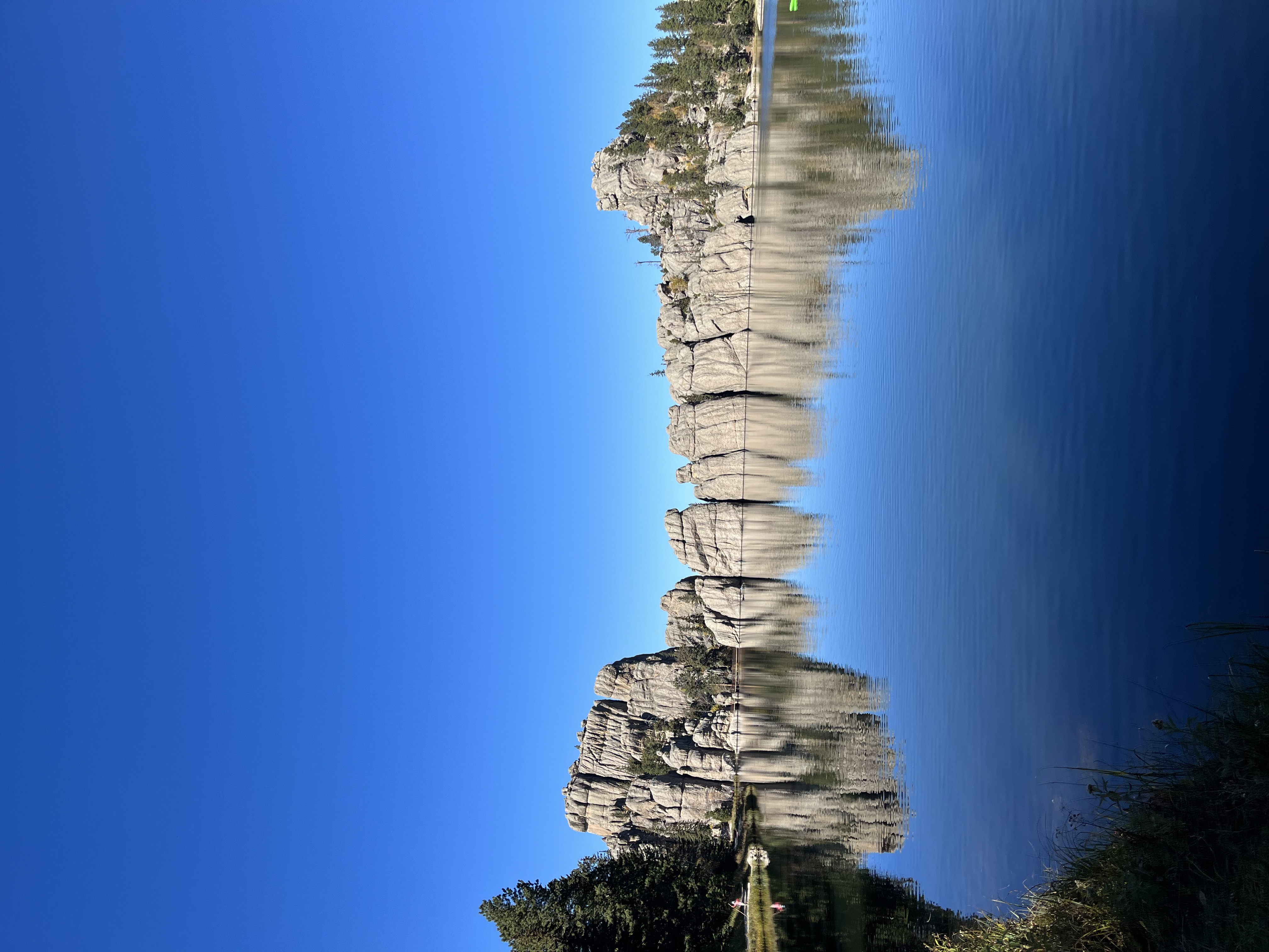 Rounded rock formations against a clear blue sky reflecting into calm water