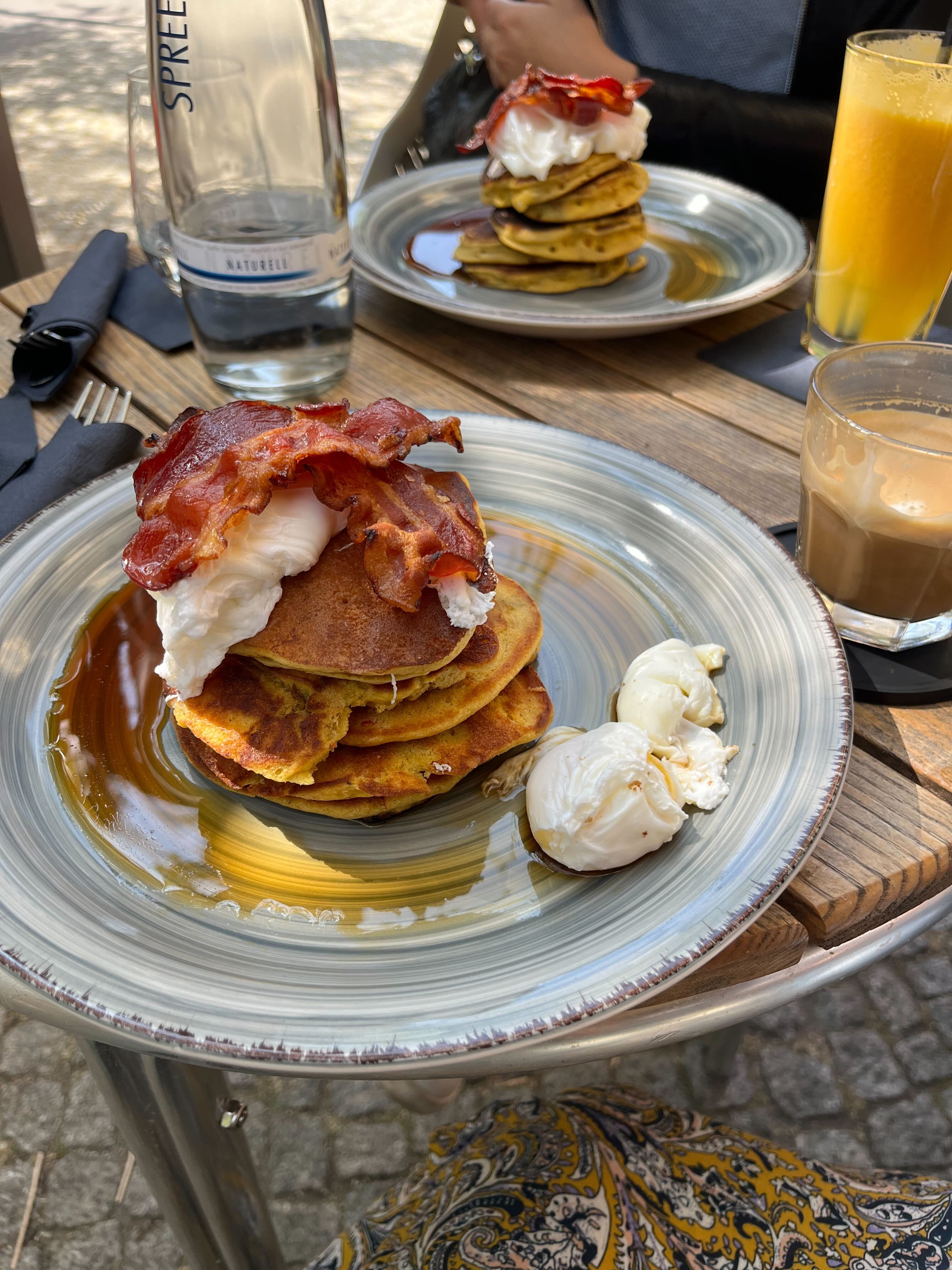 A stack of beautiful, orangey brown pancakes with eggs, bacon, and syrup